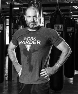 Balding grey bearded male gym trainer stands with punch bags